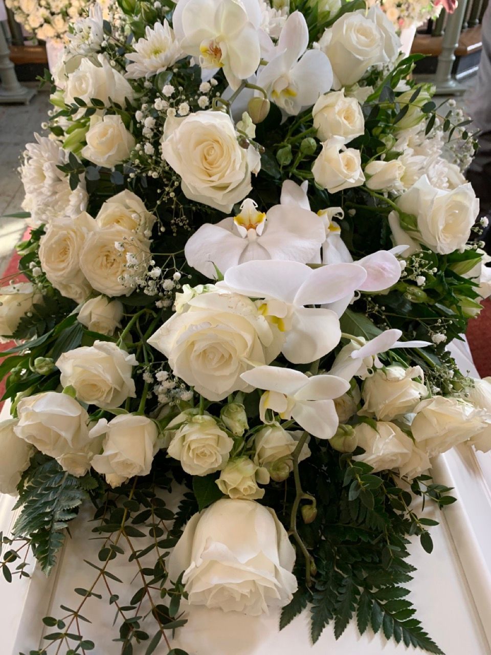 Hvit kistepynt med roser, orkidéer og brudeslør