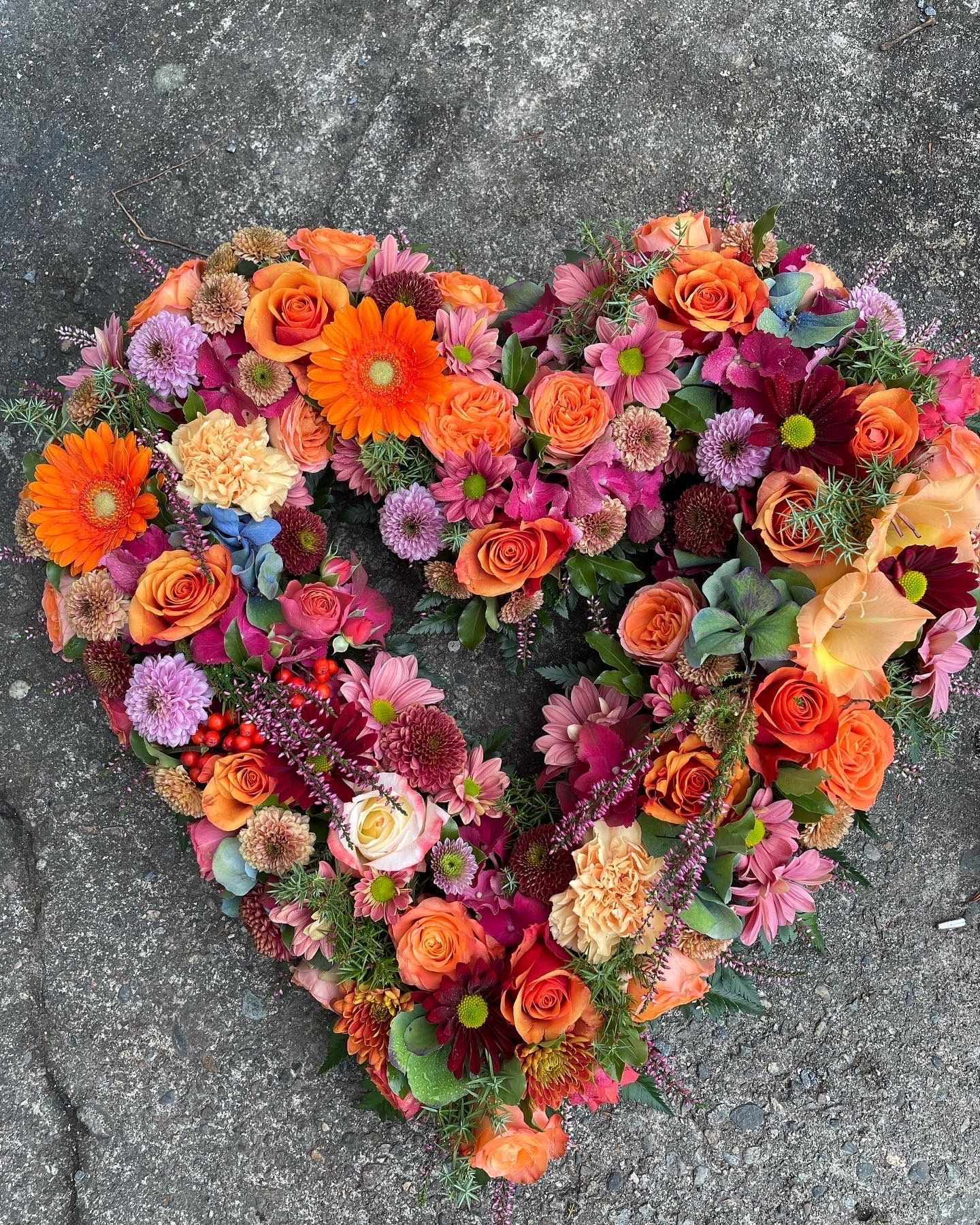 Hjerteformet sorgbukett med oransje og rosa blomster